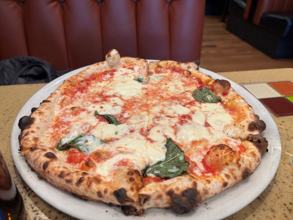 A freshly baked pizza topped with melted mozzarella cheese and fresh basil on a marble plate.