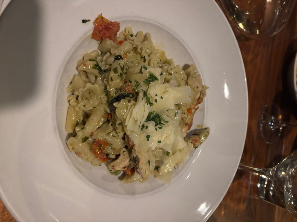 A plate of pasta topped with grated Parmesan cheese and chopped herbs, featuring a mix of ingredients including sun-dried tomatoes and pieces of chicken.