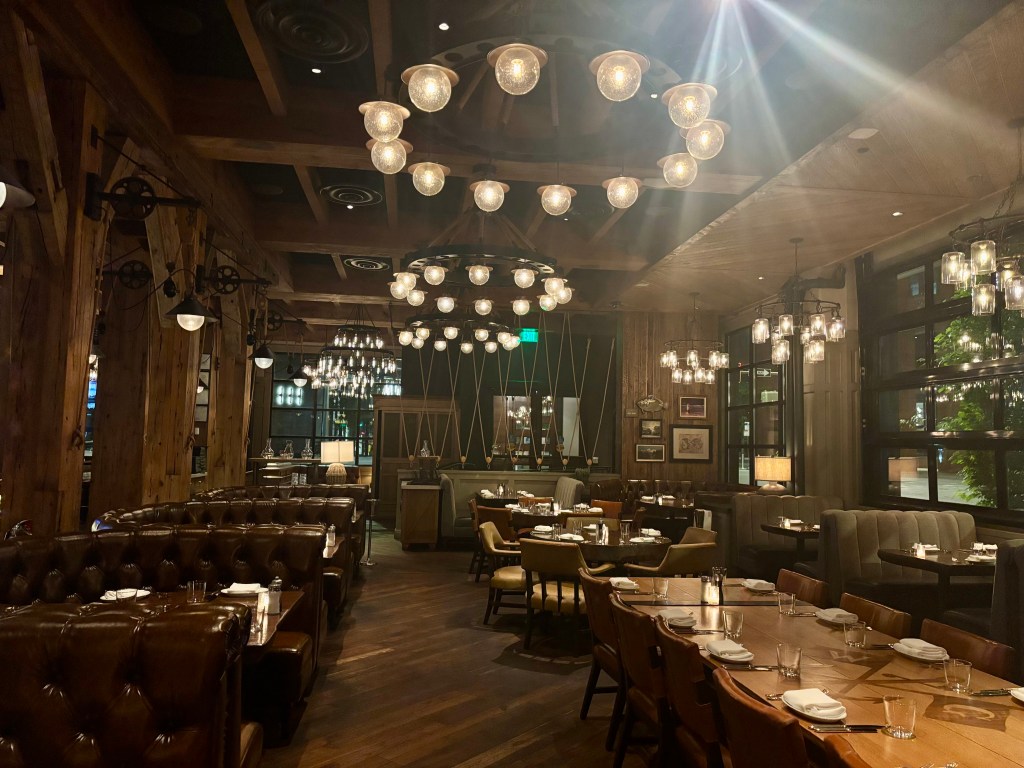 Interior of a cozy restaurant featuring wooden beams, ambient lighting from multiple pendant lamps, and plush seating arrangements.
